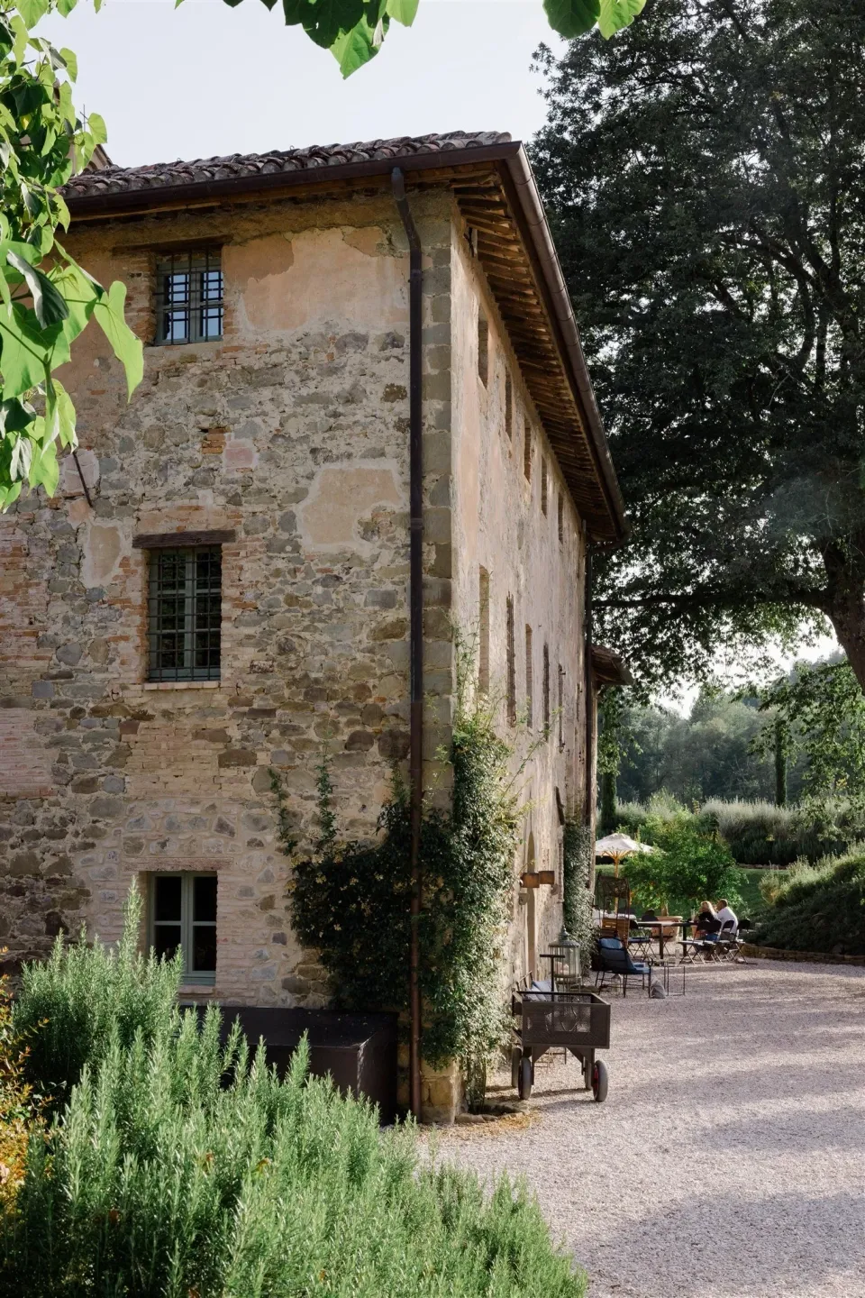 A stone country building framed by trees and clipped garden plants, in Umbria, Italy, for an Elopement Collective elopement. Photo by James from House of Love.