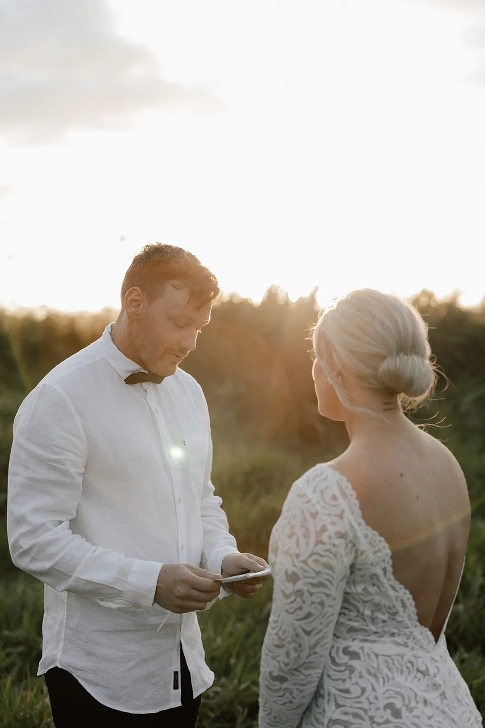 Matt reading from his vow card as Laura faces him in the evening light, in the Tweed Valley, NSW, for an Elopement Collective elopement. Photo by Bulb Creative.