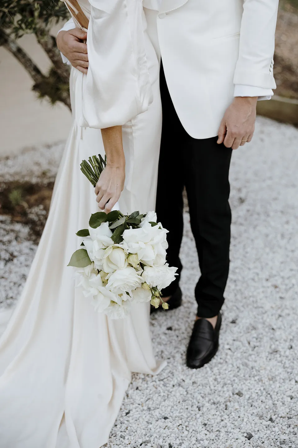 Close view of Gabrielle’s white bouquet by Mrs Gibbons and ivory Shona Joy dress beside Greg’s white Norfords jacket, at Roundhill Retreat in Obi Obi, Sunshine Coast Hinterland, Queensland, for an Elopement Collective elopement. Photo by George Bowden.