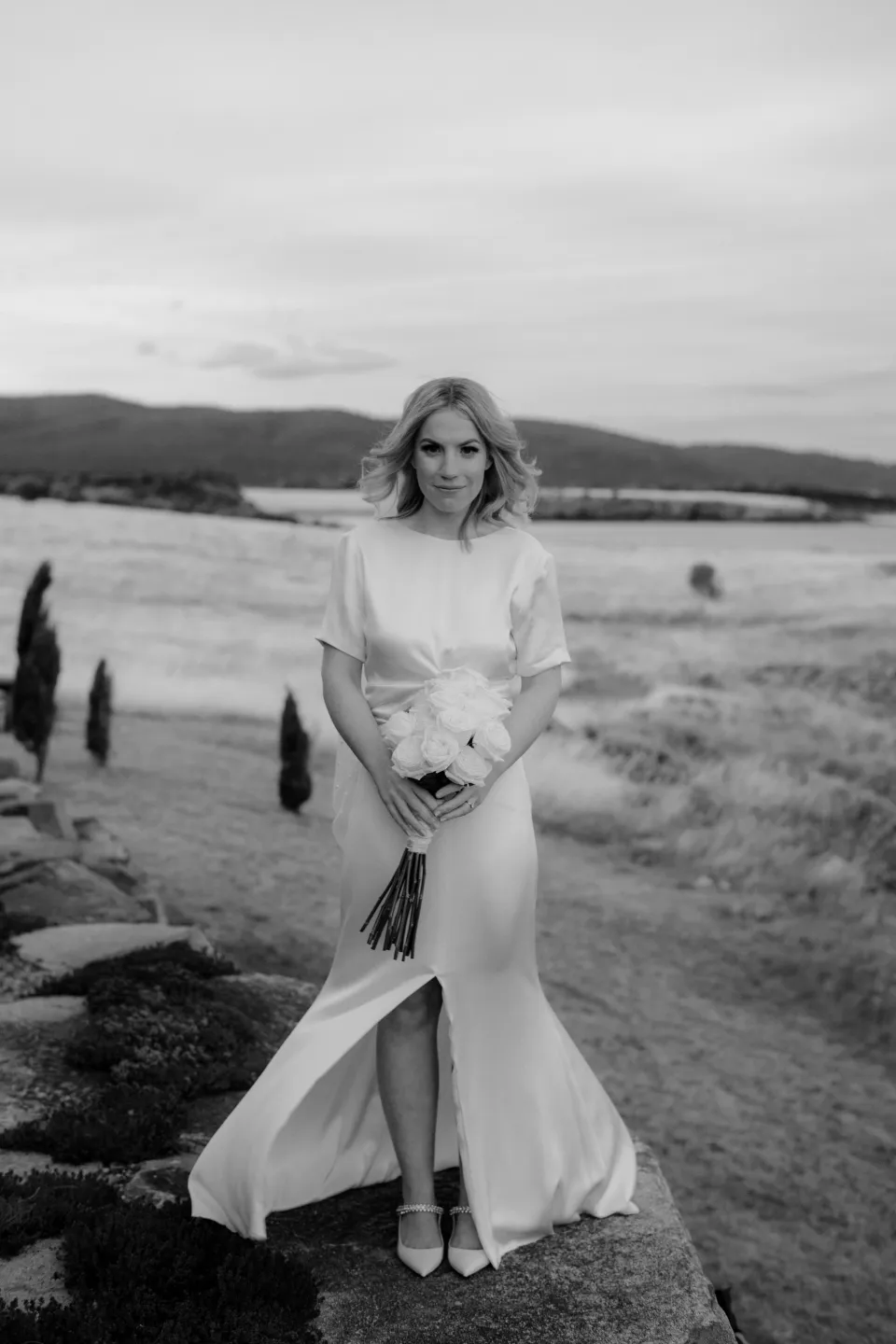 Black and white portrait of Jemmah in the coastal meadow, at Thalia Haven on the East Coast of Tasmania, Australia, for an Elopement Collective elopement. Photograph by Joey Willis.