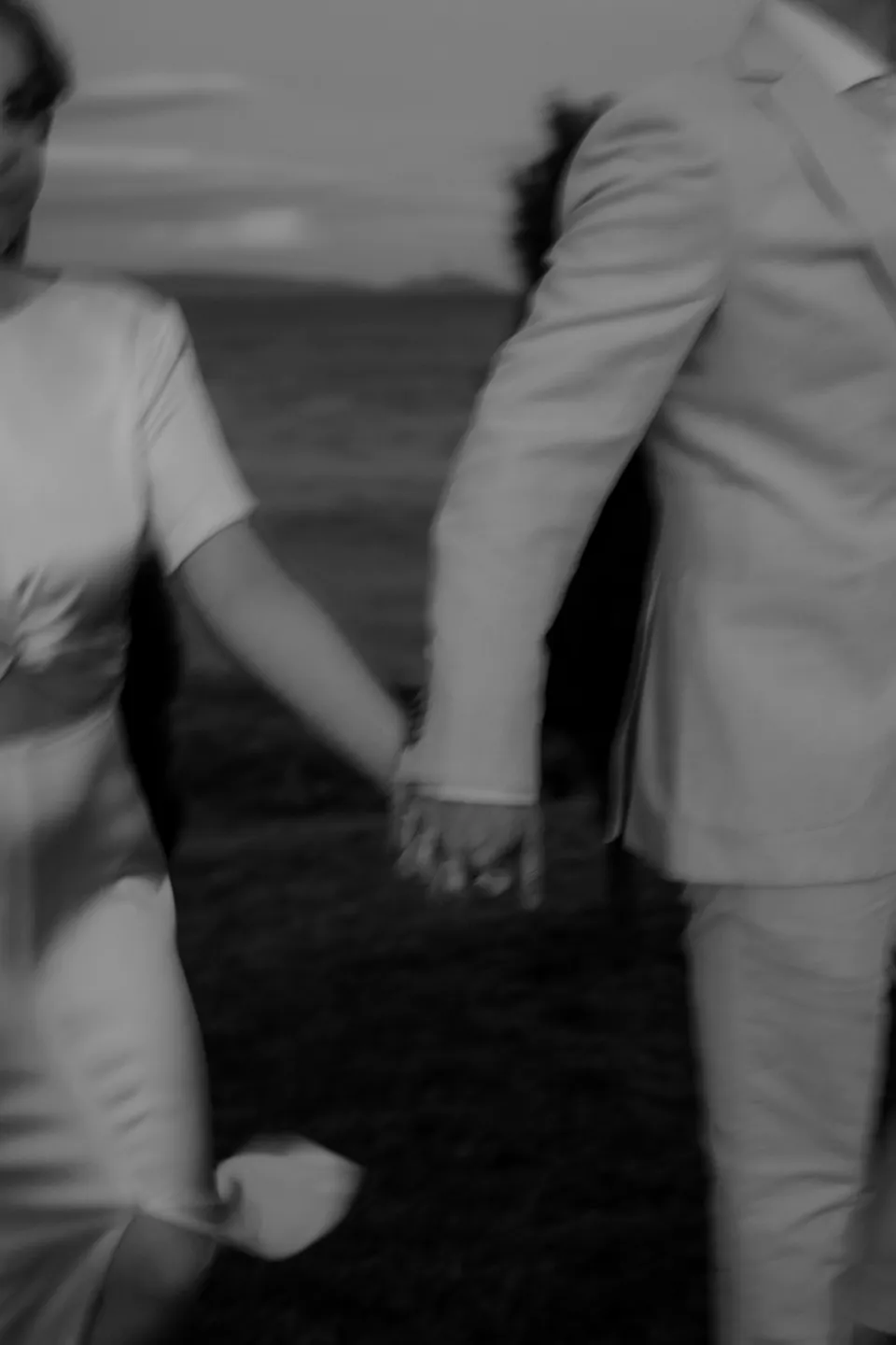 Black and white close-up of Jemmah and Jack holding hands in the meadow, at Thalia Haven on the East Coast of Tasmania, Australia, for an Elopement Collective elopement. Photograph by Joey Willis.