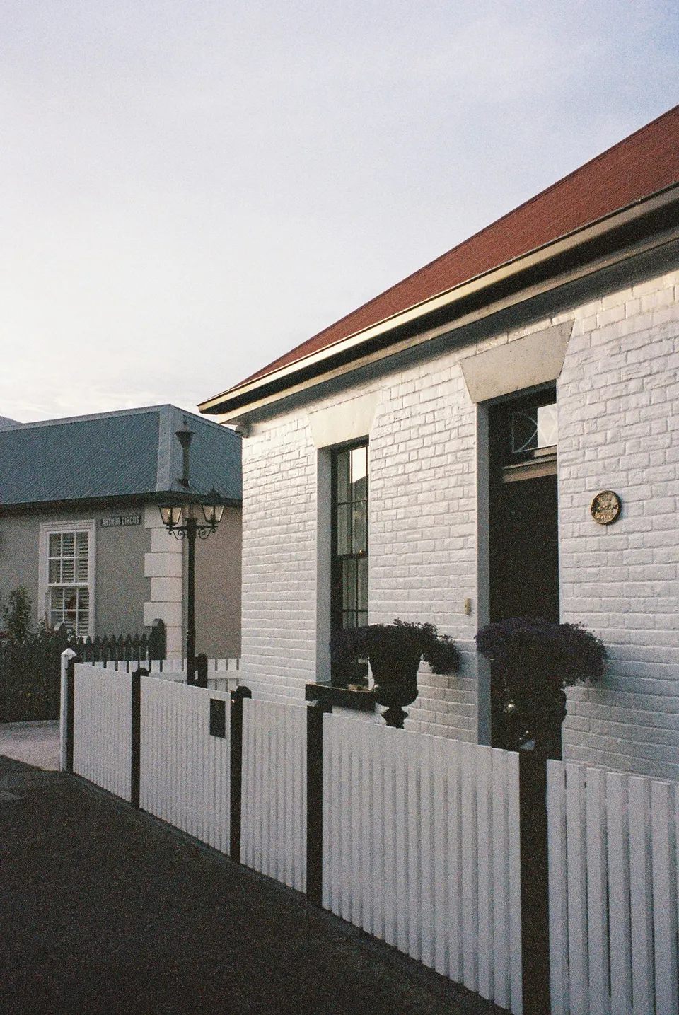 White cottages with dark doors, red and grey roofs and white picket fences lining a quiet street, at Battery Point in Hobart, Tasmania, Australia, for an Elopement Collective summer elopement. Photograph by George Bowden.