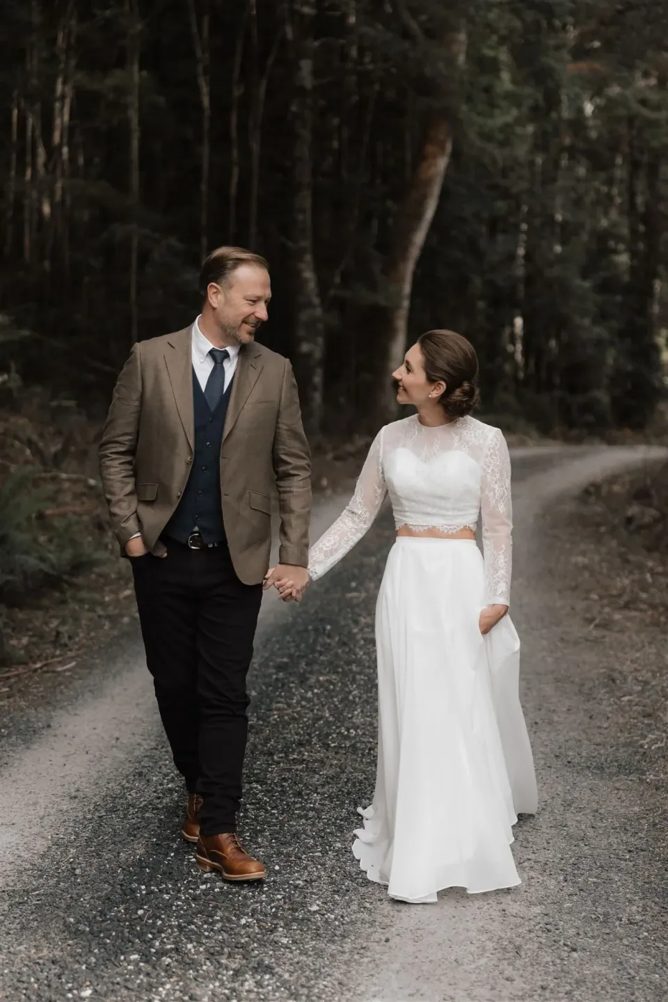 A couple walk hand in hand along a gravel track through the forest.