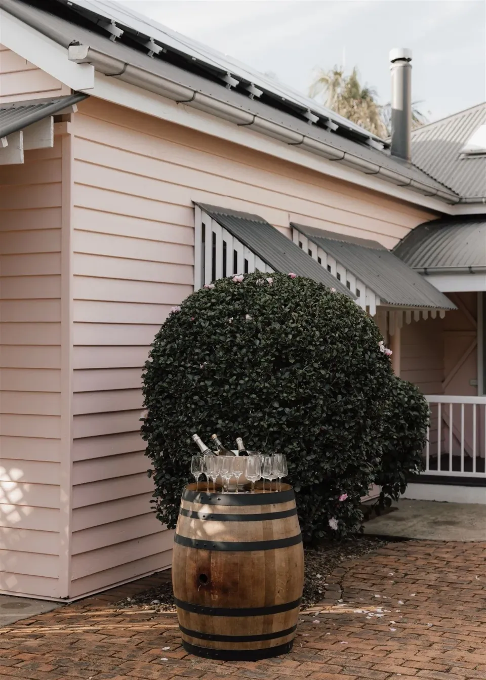 A pale weatherboard house with striped awnings, a clipped tree and a timber barrel beside the courtyard, in Montville, Sunshine Coast Hinterland, Queensland, for an Elopement Collective elopement. Photo by Bulb Creative.