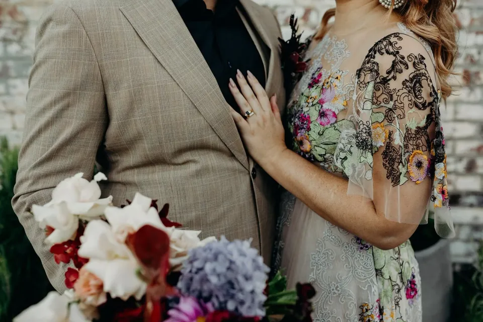 Detail of Victoria’s hand on Daniel’s beige suit, with her floral dress and bouquet by Mrs Gibbons Flowers, in Fortitude Valley, Brisbane, for an Elopement Collective elopement. Photo by Tessa Shannon.
