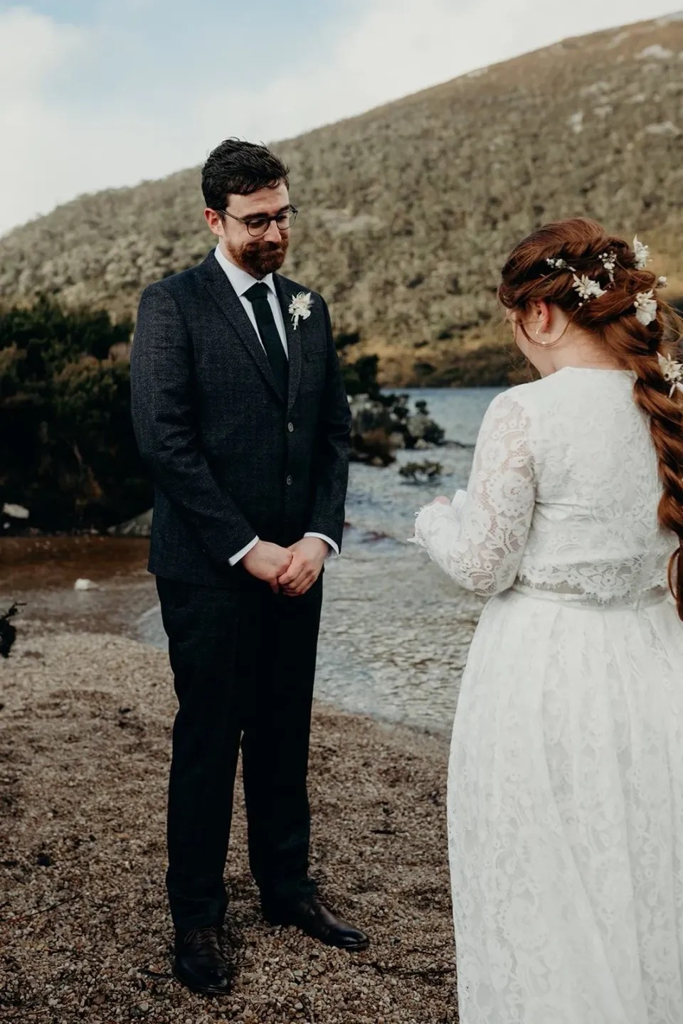 A bride reads her vows to the groom beside a mountain lake.