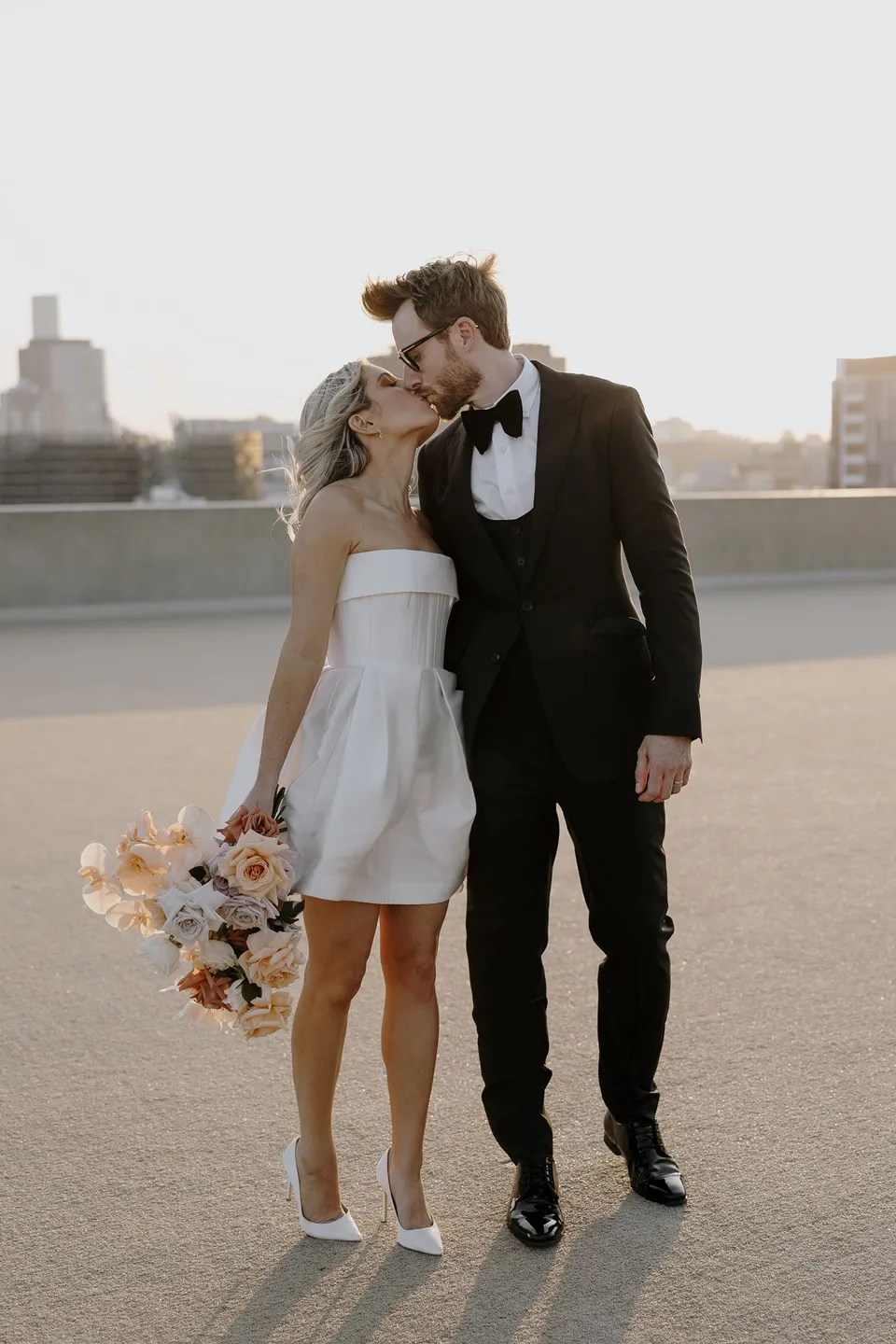 Adam kissing Danielle’s forehead as they stand hand in hand on the rooftop, at The Calile Hotel in Fortitude Valley, Brisbane, for an Elopement Collective elopement. Photo by George Bowden.
