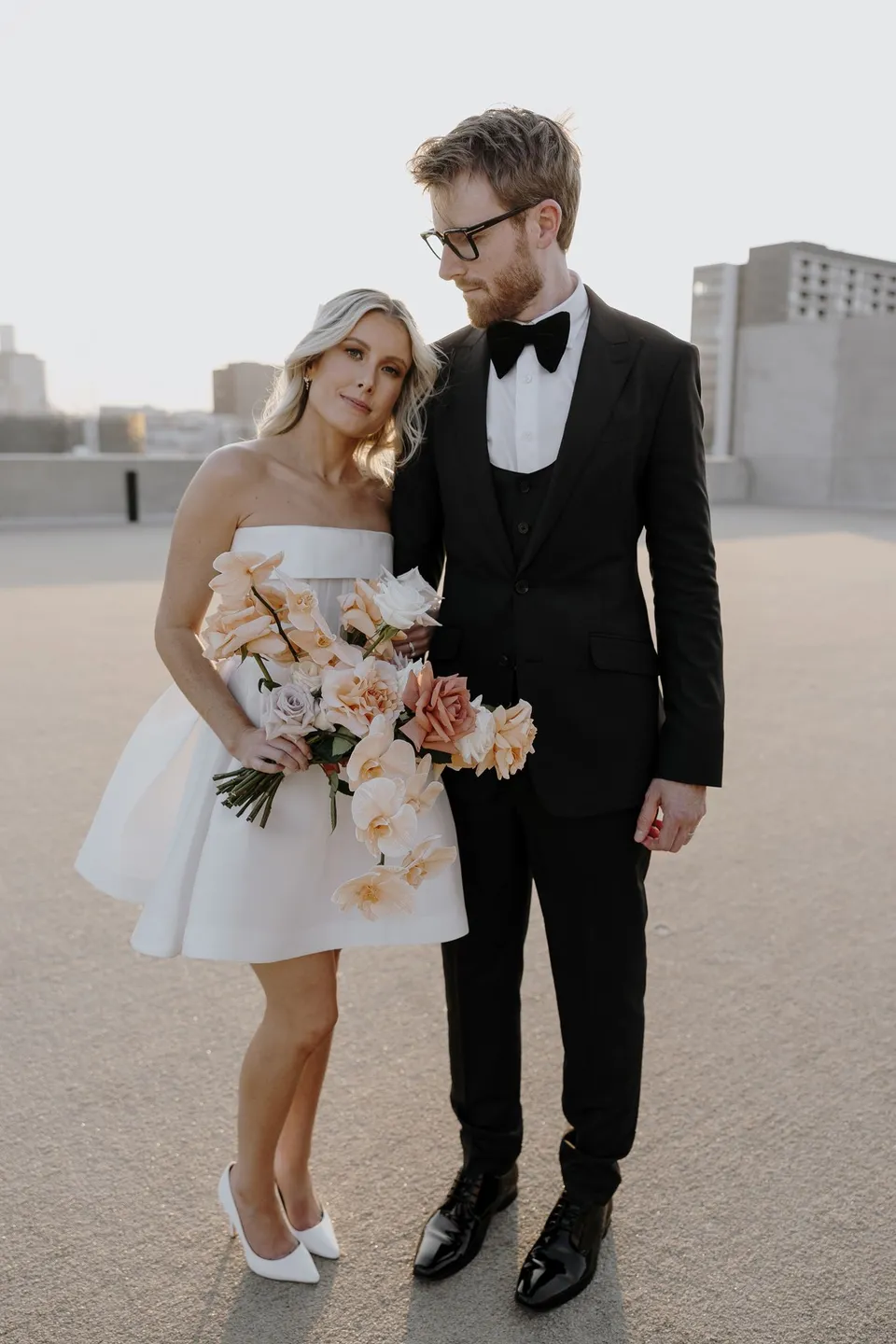 Danielle resting her head against Adam on the rooftop while holding her bouquet by Mrs Gibbons Florals, at The Calile Hotel in Fortitude Valley, Brisbane, for an Elopement Collective elopement. Photo by George Bowden.