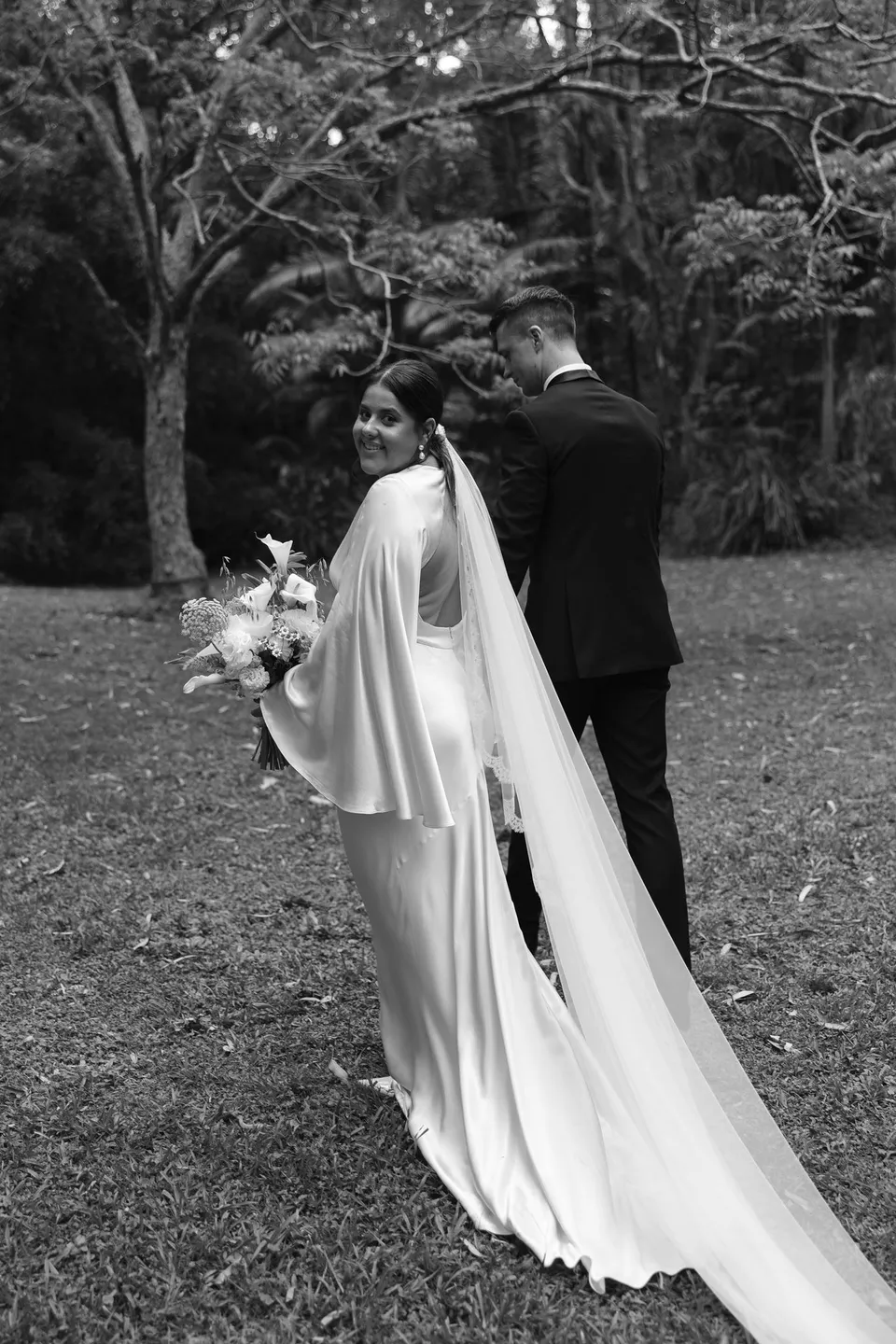 Black-and-white photograph of Matthew kissing Laura's cheek as she looks back over her shoulder. At Fig Tree Villa in Ewingsdale, Byron Bay, for an Elopement Collective elopement. Photograph by George Bowden.