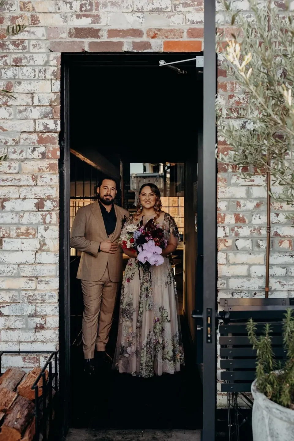 Victoria and Daniel standing together in a doorway framed by weathered brick walls, in Fortitude Valley, Brisbane, for an Elopement Collective elopement. Photo by Tessa Shannon.