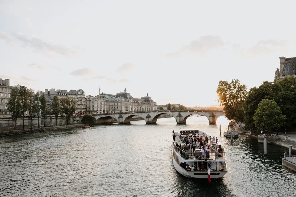 A sightseeing boat carrying passengers along the Seine towards an arched bridge, beside the Seine in Paris, France, during an Elopement Collective elopement. Photograph by George Bowden.