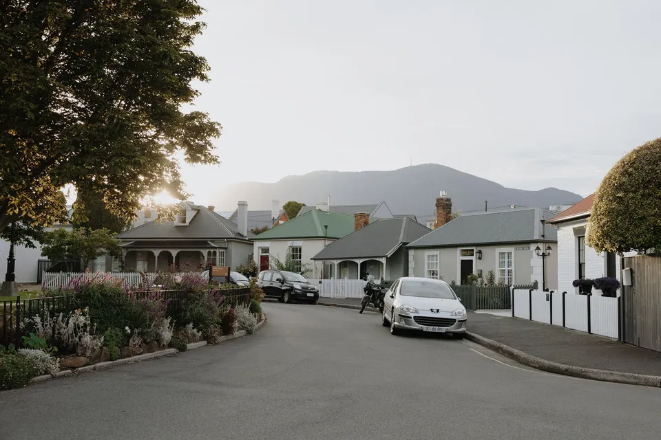 A curved street at Arthur Circus lined with cottages, picket fences and gardens, with the mountain rising beyond, at Arthur Circus in Battery Point, Hobart, Tasmania, Australia, for an Elopement Collective summer elopement. Photograph by George Bowden.