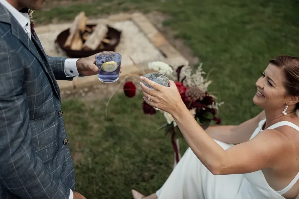 A couple raise their glasses beside an outdoor fire after their elopement.