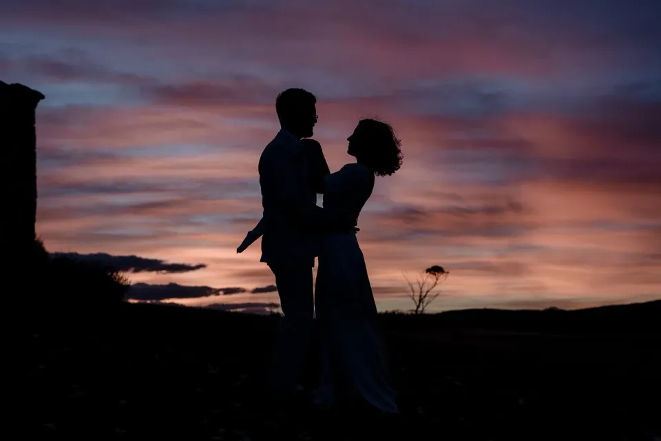 A couple are silhouetted against a vivid pink and purple sunset.