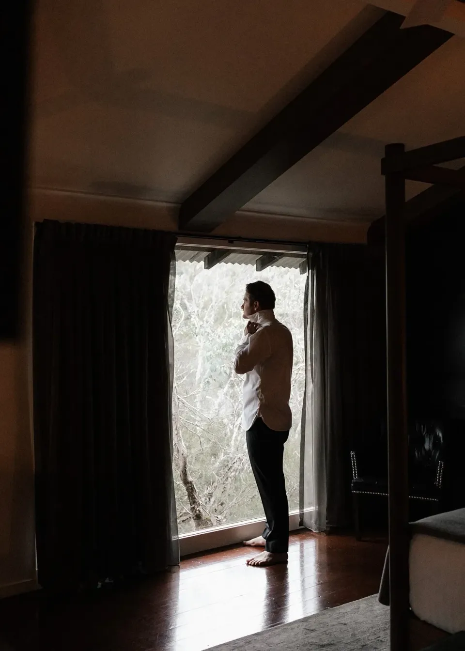 A person stands in silhouette at a cabin window overlooking the water.