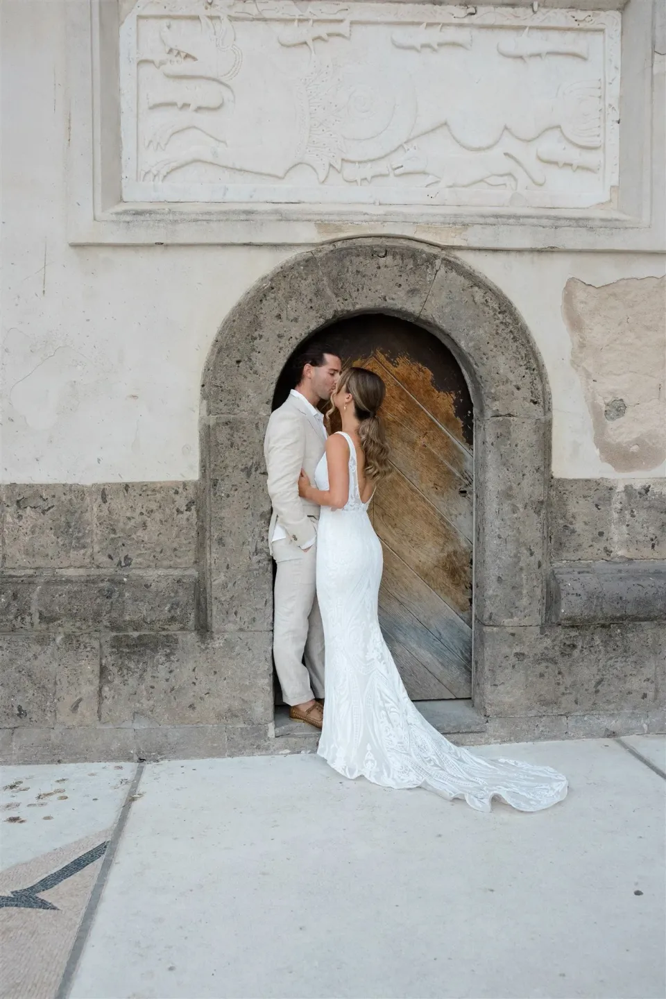 Sarah and Josh kissing in a narrow arched doorway, her white dress trailing across the paving, in Positano on Italy’s Amalfi Coast, for an Elopement Collective elopement. Photo by James from House of Love.
