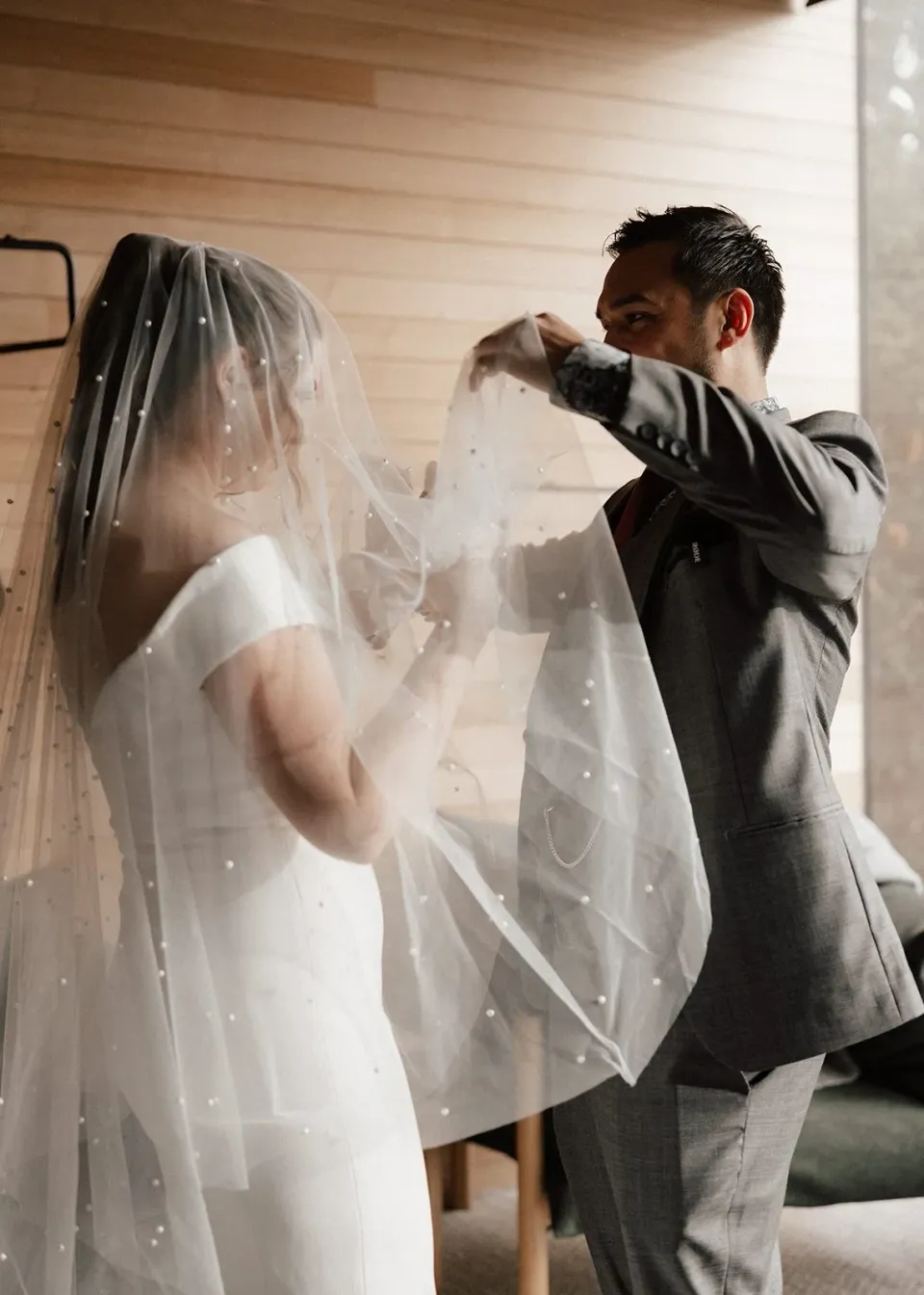 Jono helping Sarah arrange her long veil inside their timber-lined accommodation, at Pumphouse Point, Lake St Clair, Tasmania, for an Elopement Collective elopement. Photo by Bulb Creative.
