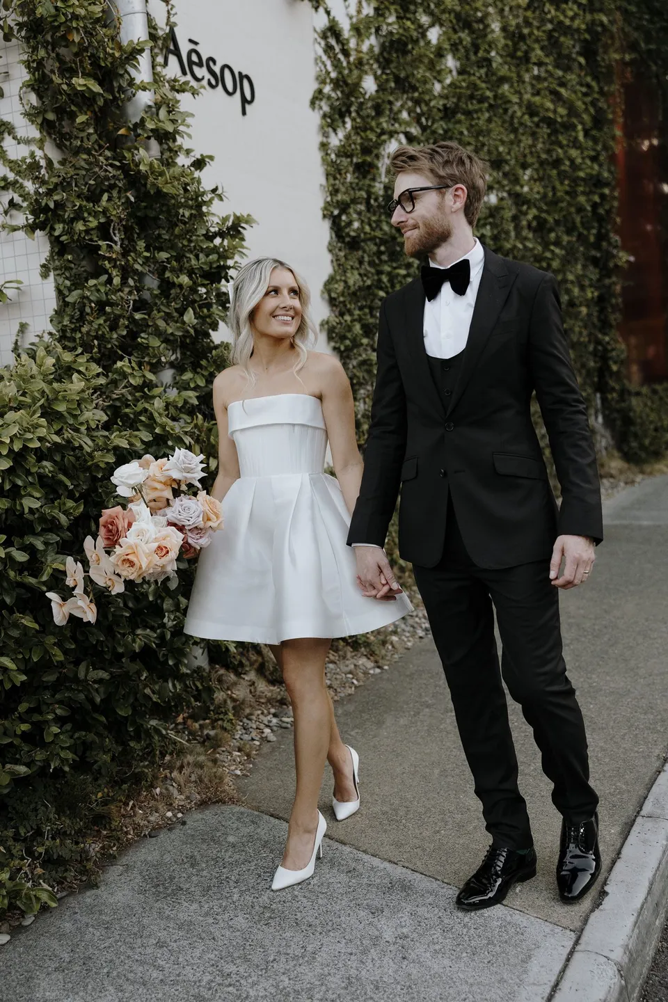 Danielle and Adam laughing and holding hands beside an ivy wall in the James Street precinct, in the James Street precinct, Fortitude Valley, Brisbane, for an Elopement Collective elopement. Photo by George Bowden.