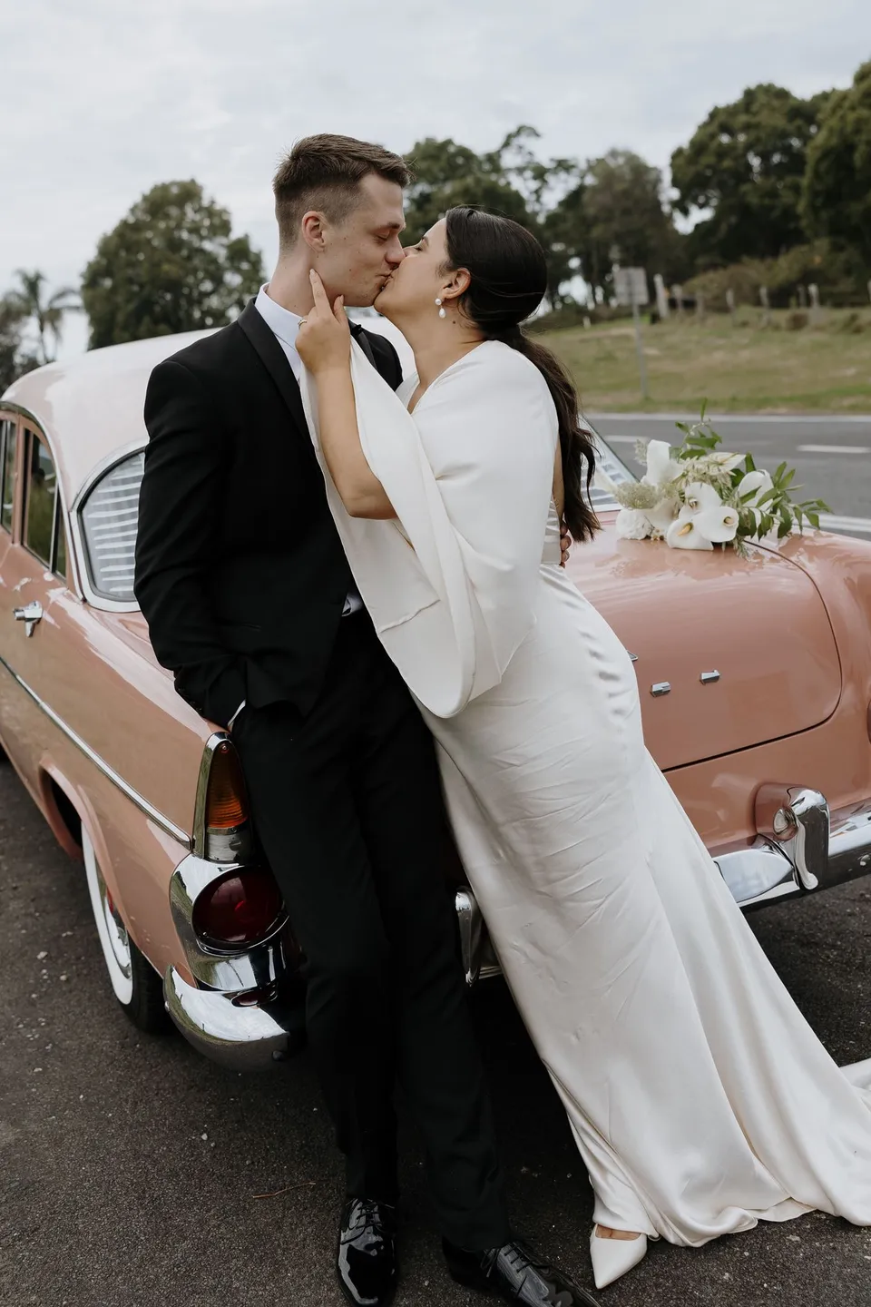 Laura and Matthew kissing beside the pink Holden from May The E.K. In the Byron Bay region of northern New South Wales, for an Elopement Collective elopement. Photograph by George Bowden.