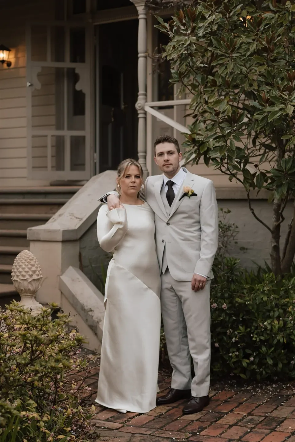 Maddy and Cameron standing together beside the house veranda, with her hand resting on his shoulder, at The Mayor’s Residence in Daylesford, Victoria, for an Elopement Collective elopement. Photo by Bulb Creative.
