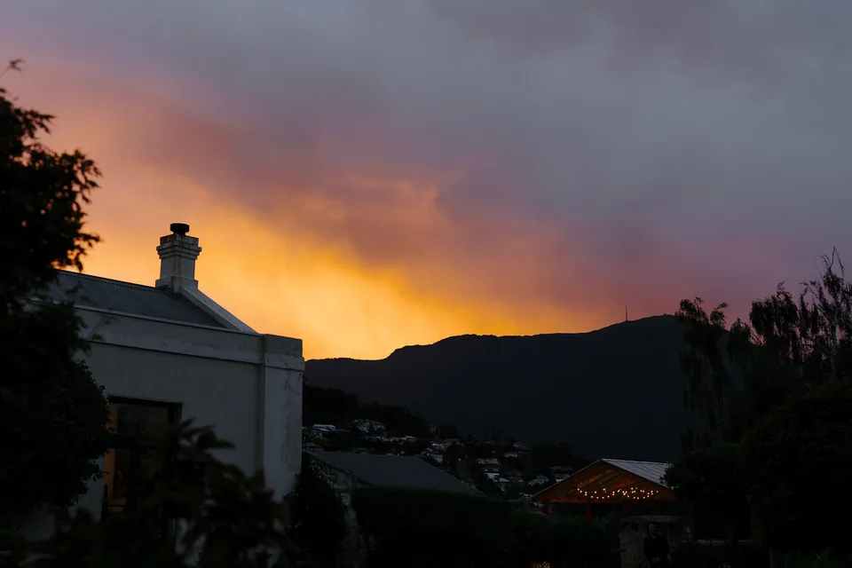 Orange and pink sunset clouds glowing above the dark mountain ridge and the hotel’s roofs, at Islington Hotel in South Hobart, Tasmania, Australia, for an Elopement Collective summer elopement. Photograph by George Bowden.