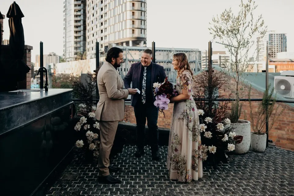 Daniel reading his vows to Victoria with celebrant Josh Withers beside them, at Agnes Restaurant in Fortitude Valley, Brisbane, for an Elopement Collective elopement. Photo by Tessa Shannon.