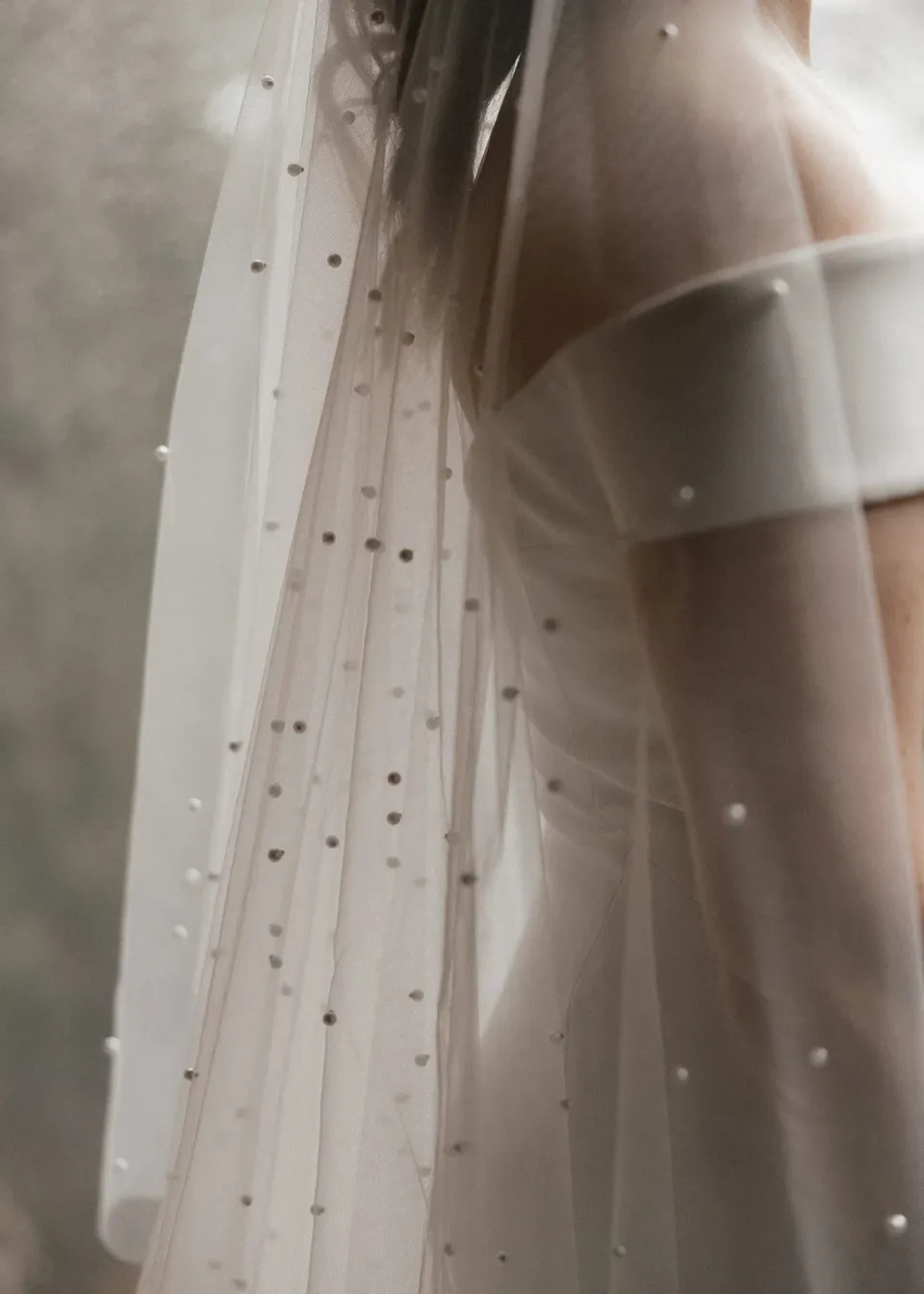 Close view of Sarah’s off-the-shoulder white dress beneath a sheer veil dotted with small pearls, at Pumphouse Point, Lake St Clair, Tasmania, for an Elopement Collective elopement. Photo by Bulb Creative.