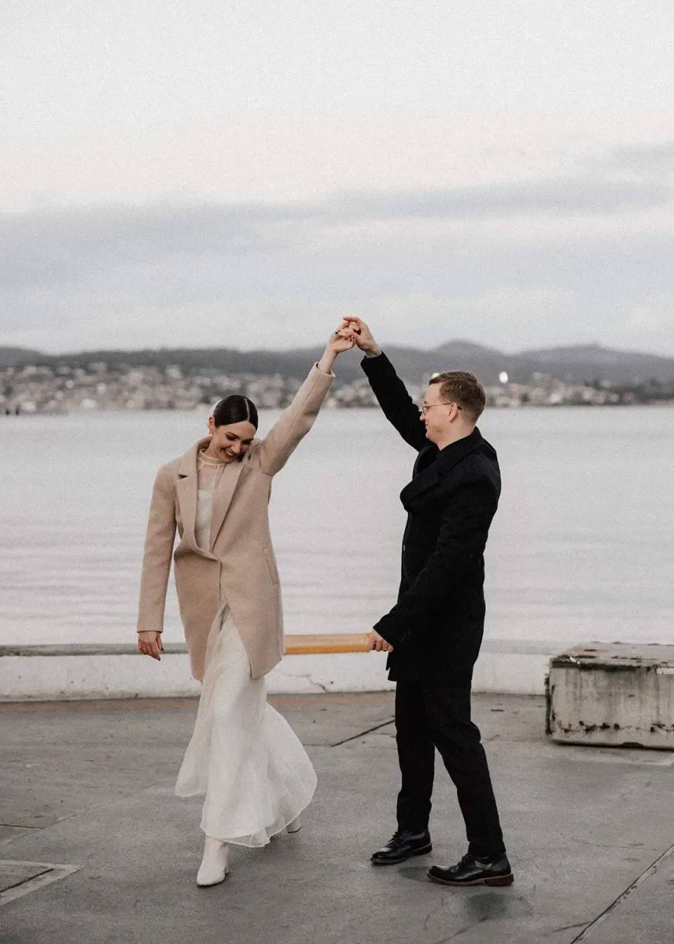 A groom twirls his bride on a waterfront terrace overlooking the river.