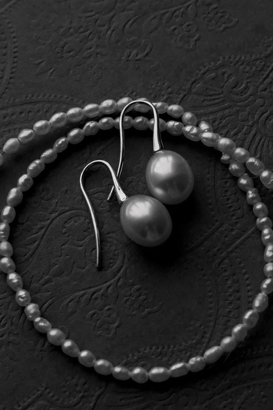 Black-and-white close-up of pearl earrings and a beaded necklace on a textured surface, in Umbria, Italy, for an Elopement Collective elopement. Photo by James from House of Love.