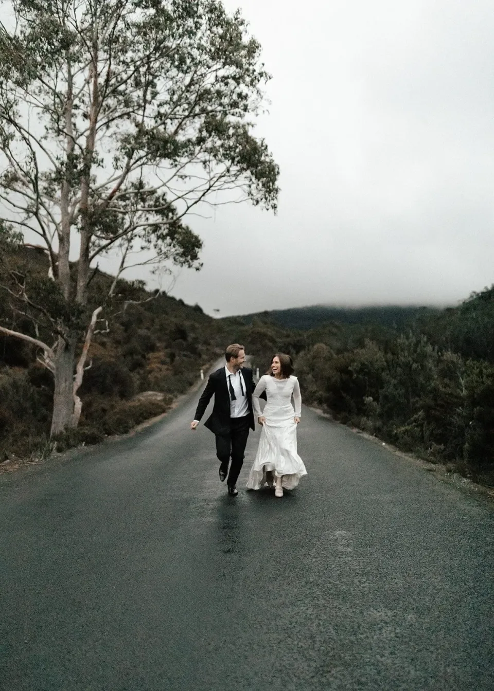 A couple walk together along a quiet road through bushland.