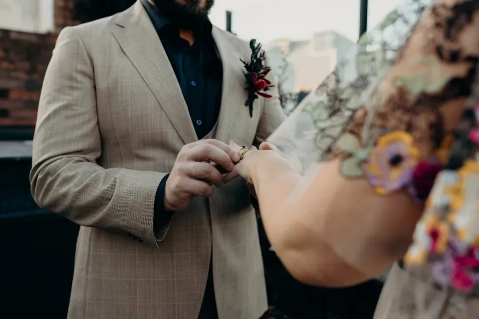 Close-up of Daniel placing a wedding ring on Victoria’s finger, with his beige suit and her floral dress visible, at Agnes Restaurant in Fortitude Valley, Brisbane, for an Elopement Collective elopement. Photo by Tessa Shannon.
