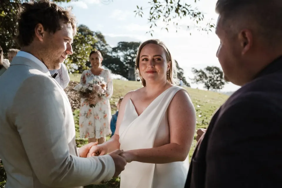 Alyce listening and holding Andrew’s hands during their ceremony with Josh Withers, at Observatory Hill in Sydney, New South Wales, for an Elopement Collective elopement. Photo by Jason Corroto.