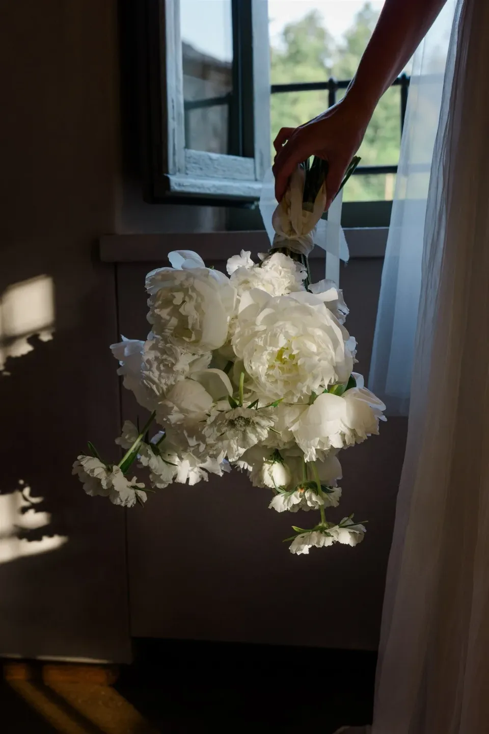Close view of Shelby holding her white bouquet by Le Francesche beside a sunlit window, in Umbria, Italy, for an Elopement Collective elopement. Photo by James from House of Love.