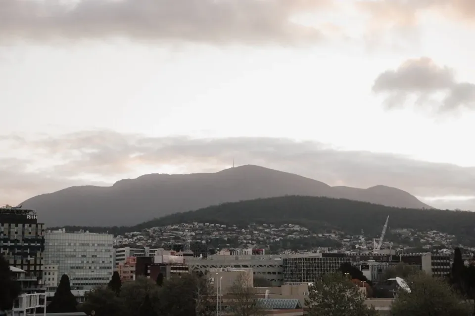 Hobart rooftops beneath kunanyi/Mount Wellington and a cloudy evening sky.