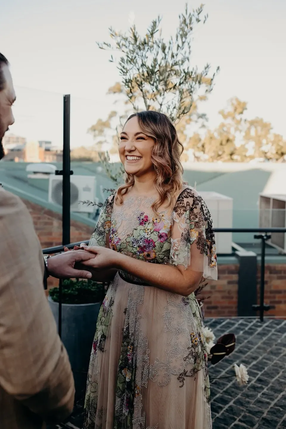 Victoria smiling as she holds Daniel’s hand during their rooftop ceremony, at Agnes Restaurant in Fortitude Valley, Brisbane, for an Elopement Collective elopement. Photo by Tessa Shannon.