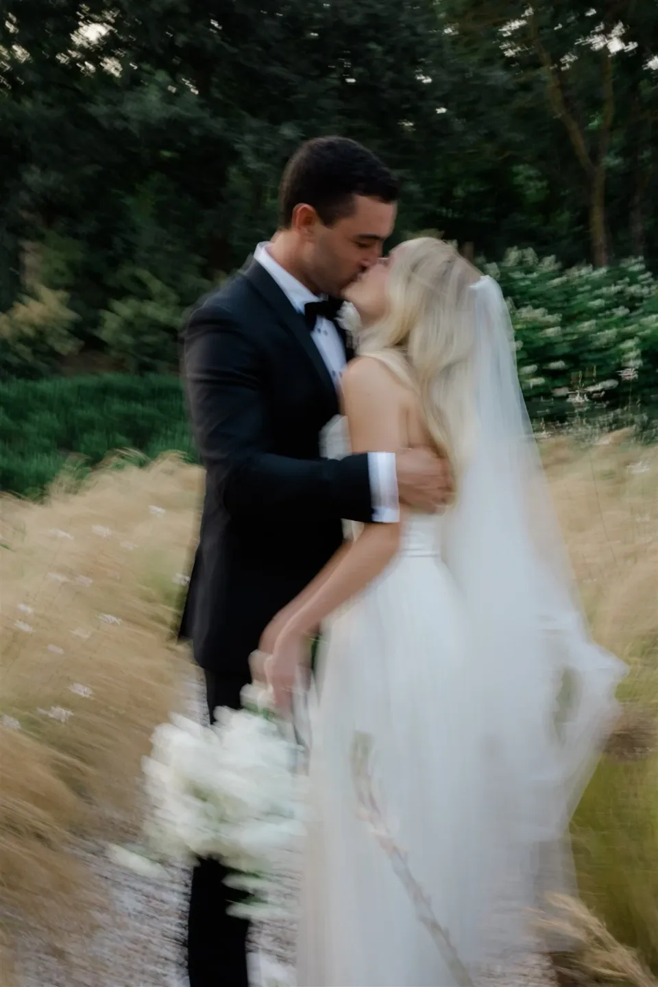 Softly blurred portrait of Shelby and Jack kissing in a grassy garden, her white bouquet by Le Francesche at her side, in Umbria, Italy, for an Elopement Collective elopement. Photo by James from House of Love.