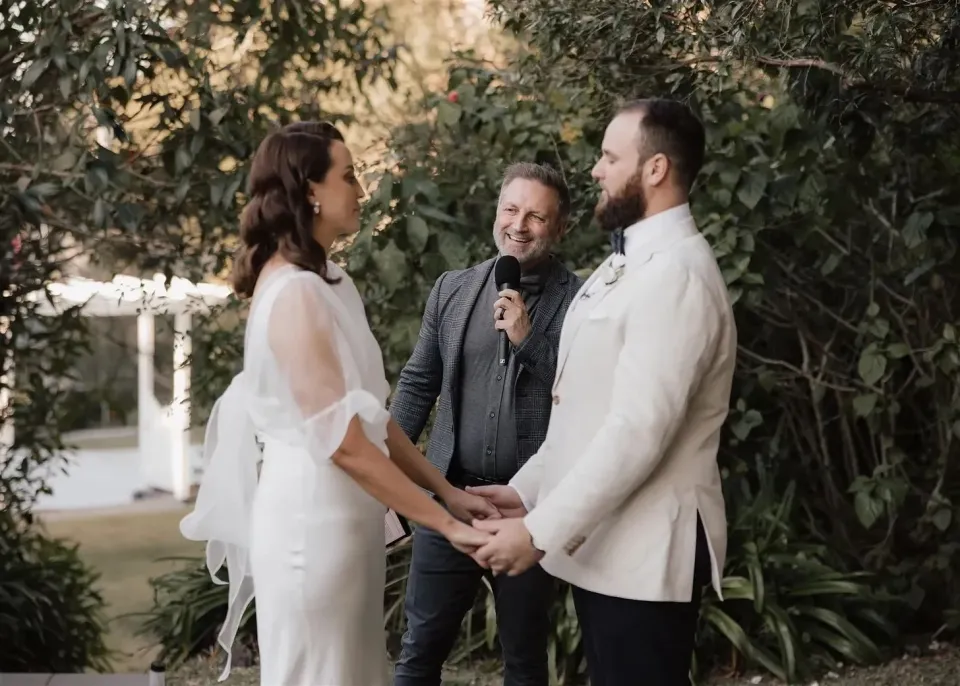 Tineeka and Chris holding hands and smiling during their ceremony with celebrant Jake Smith, in Montville, Sunshine Coast Hinterland, Queensland, for an Elopement Collective elopement. Photo by Bulb Creative.