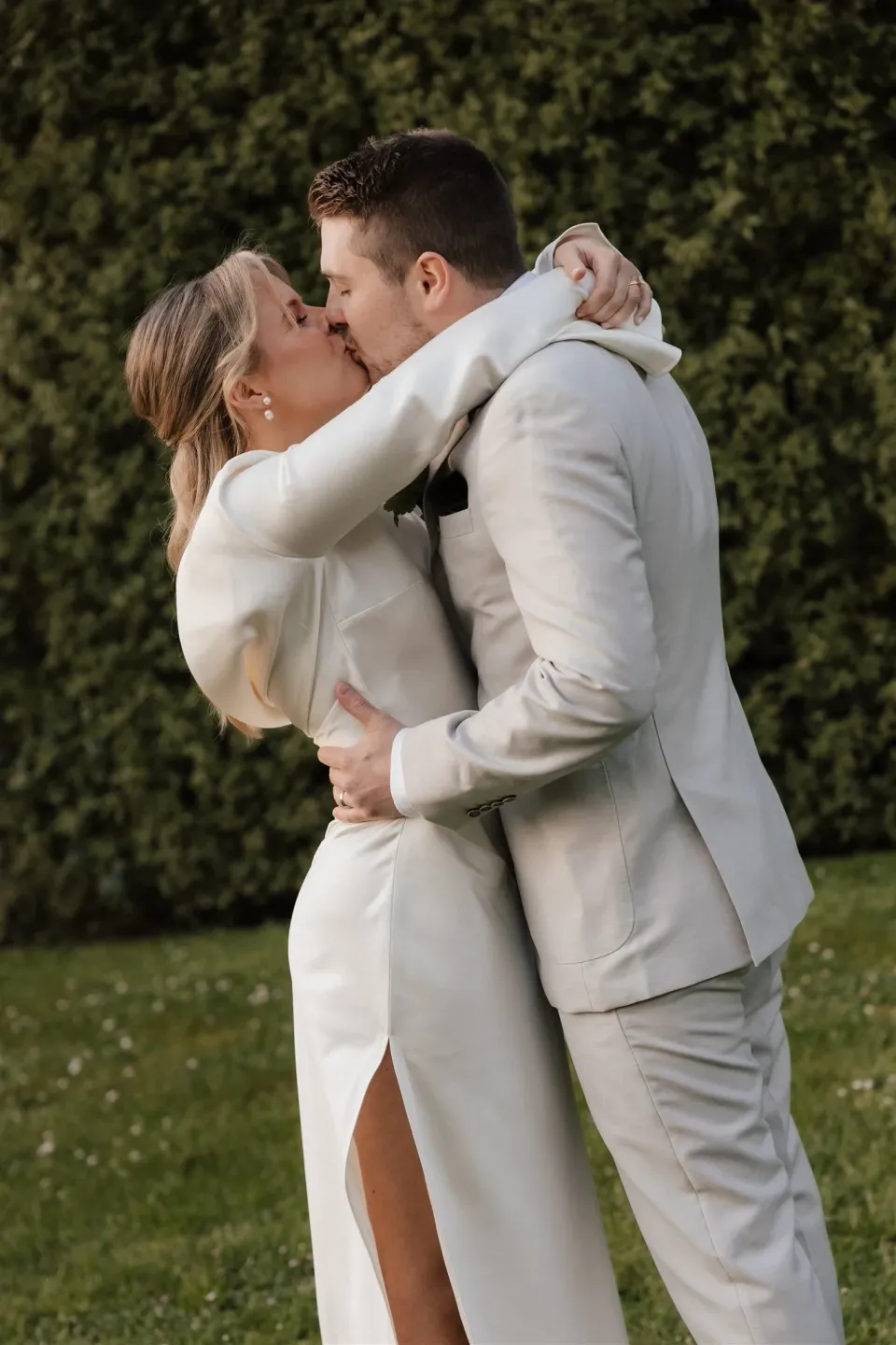 Maddy and Cameron embracing and kissing beside a tall garden hedge, at The Mayor’s Residence in Daylesford, Victoria, for an Elopement Collective elopement. Photo by Bulb Creative.