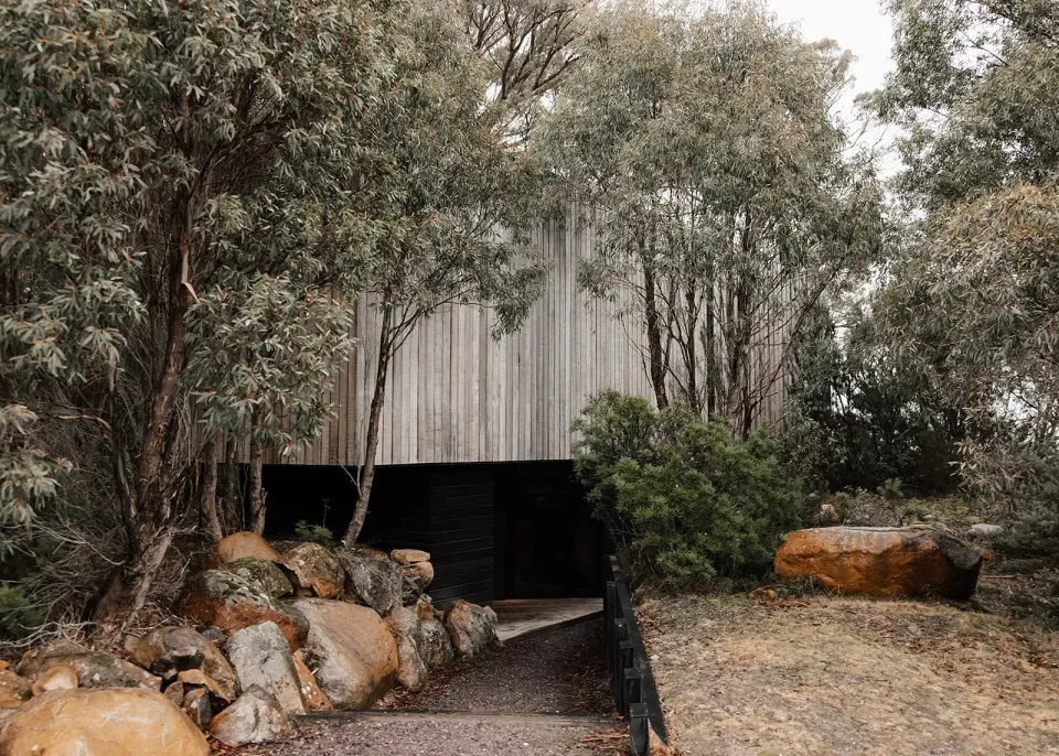 A small timber cabin nestled among trees and boulders, at Pumphouse Point, Lake St Clair, Tasmania, for an Elopement Collective elopement. Photo by Bulb Creative.