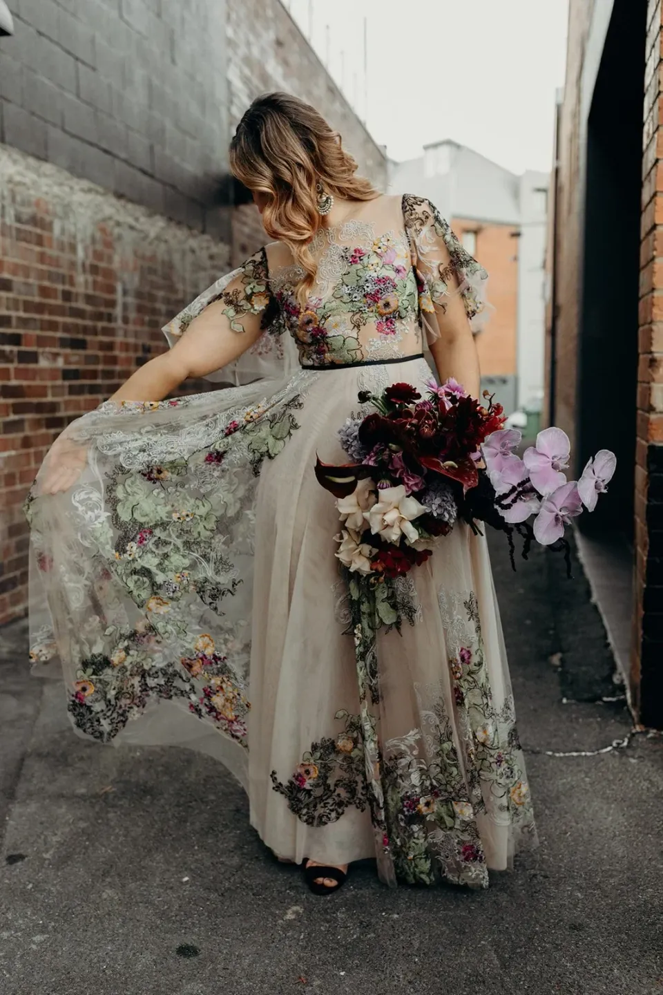 Victoria looking down at her flowing floral dress while holding her bouquet by Mrs Gibbons Flowers, in Fortitude Valley, Brisbane, for an Elopement Collective elopement. Photo by Tessa Shannon.