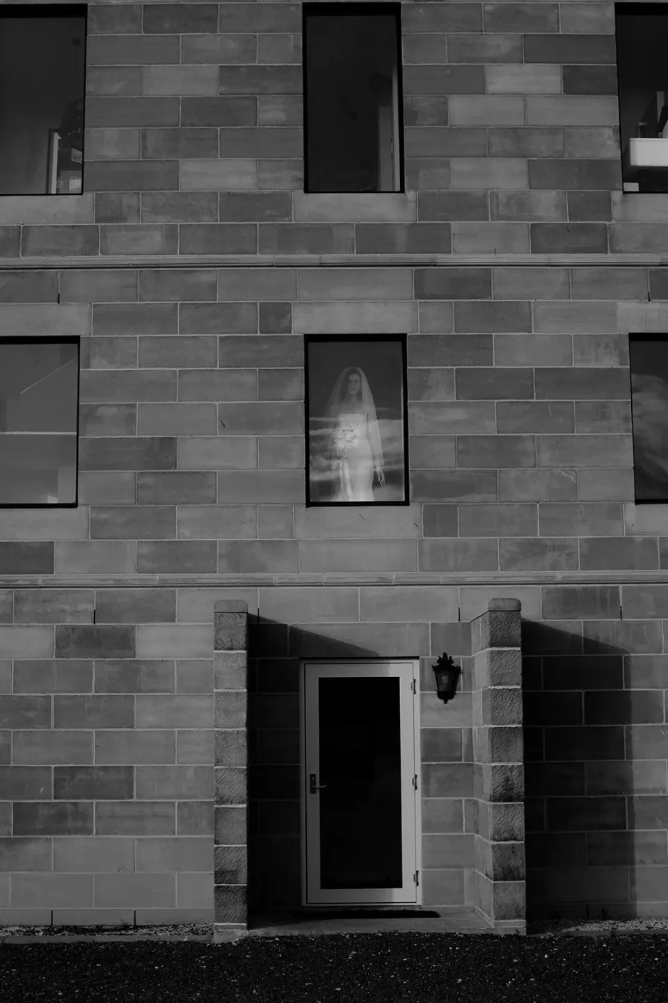 A black-and-white photograph of a sandstone building with tall windows and an open doorway.