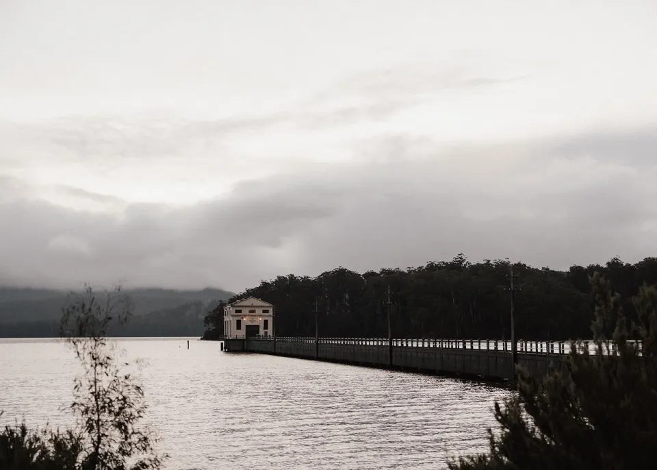 The Pumphouse Point building at the end of its long jetty, with forested hills across the lake, at Pumphouse Point, Lake St Clair, Tasmania, for an Elopement Collective elopement. Photo by Bulb Creative.