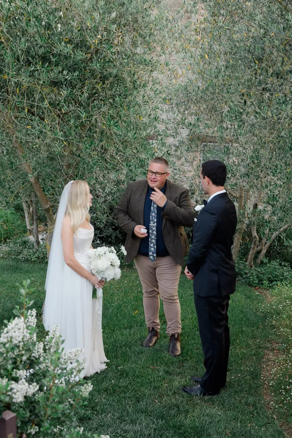 Jack speaking to Shelby during their garden ceremony as Josh Withers holds the microphone, in Umbria, Italy, for an Elopement Collective elopement. Photo by James from House of Love.