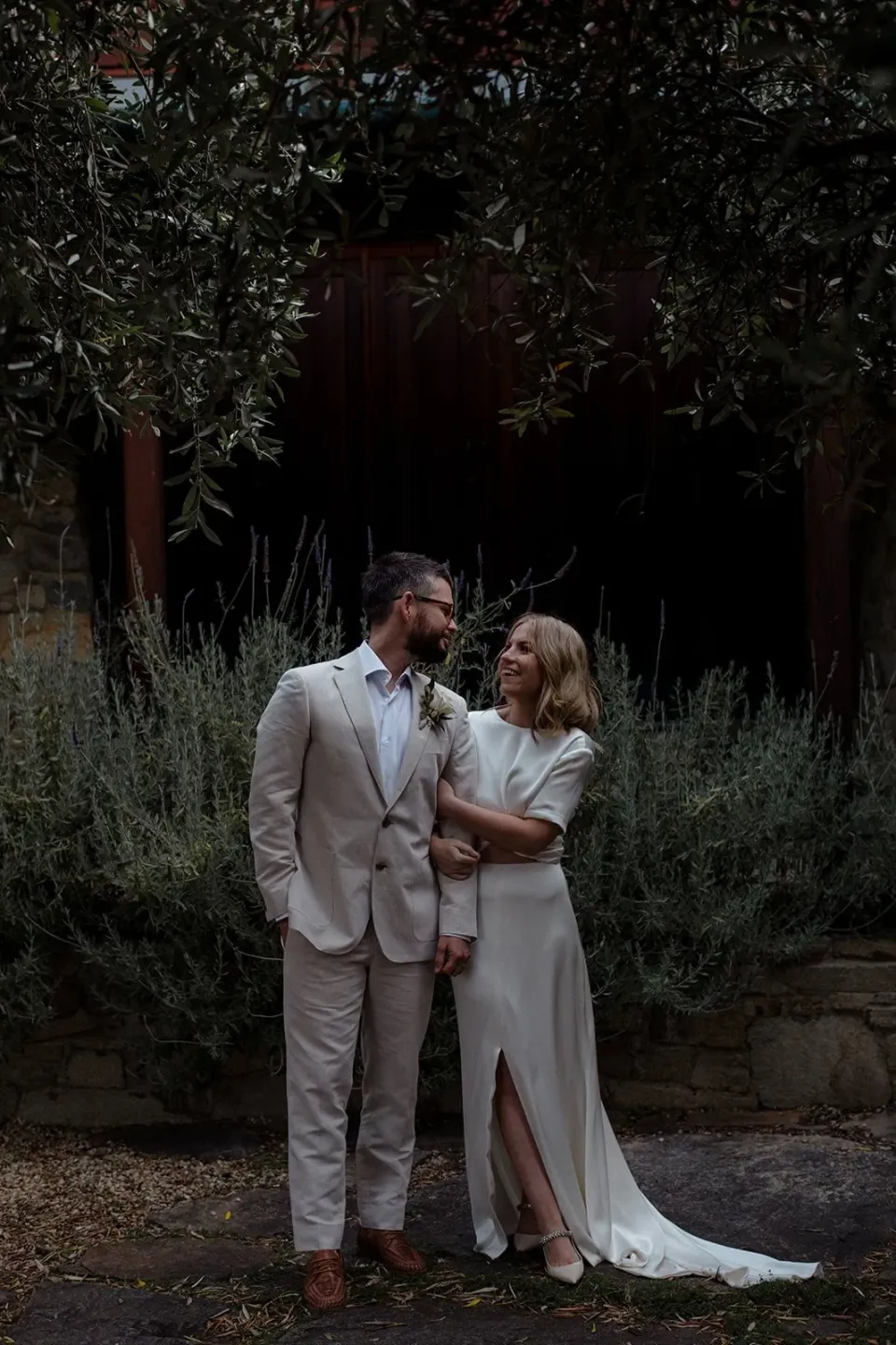 A couple embrace on a garden path surrounded by dark foliage.