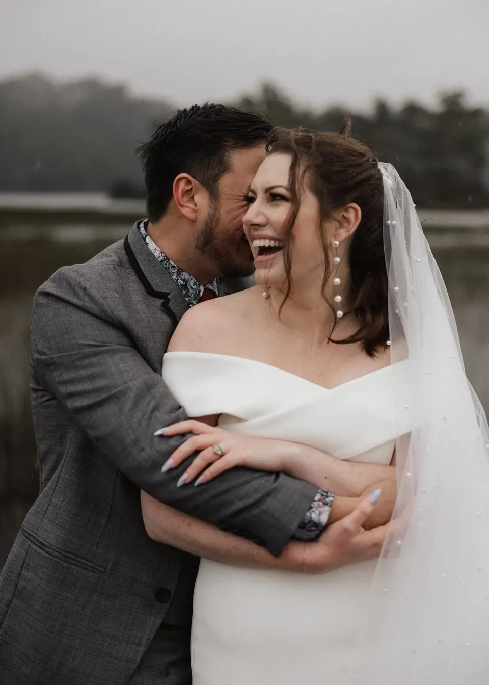 Sarah laughing as Jono kisses her cheek beside the lake, at Pumphouse Point, Lake St Clair, Tasmania, for an Elopement Collective elopement. Photo by Bulb Creative.