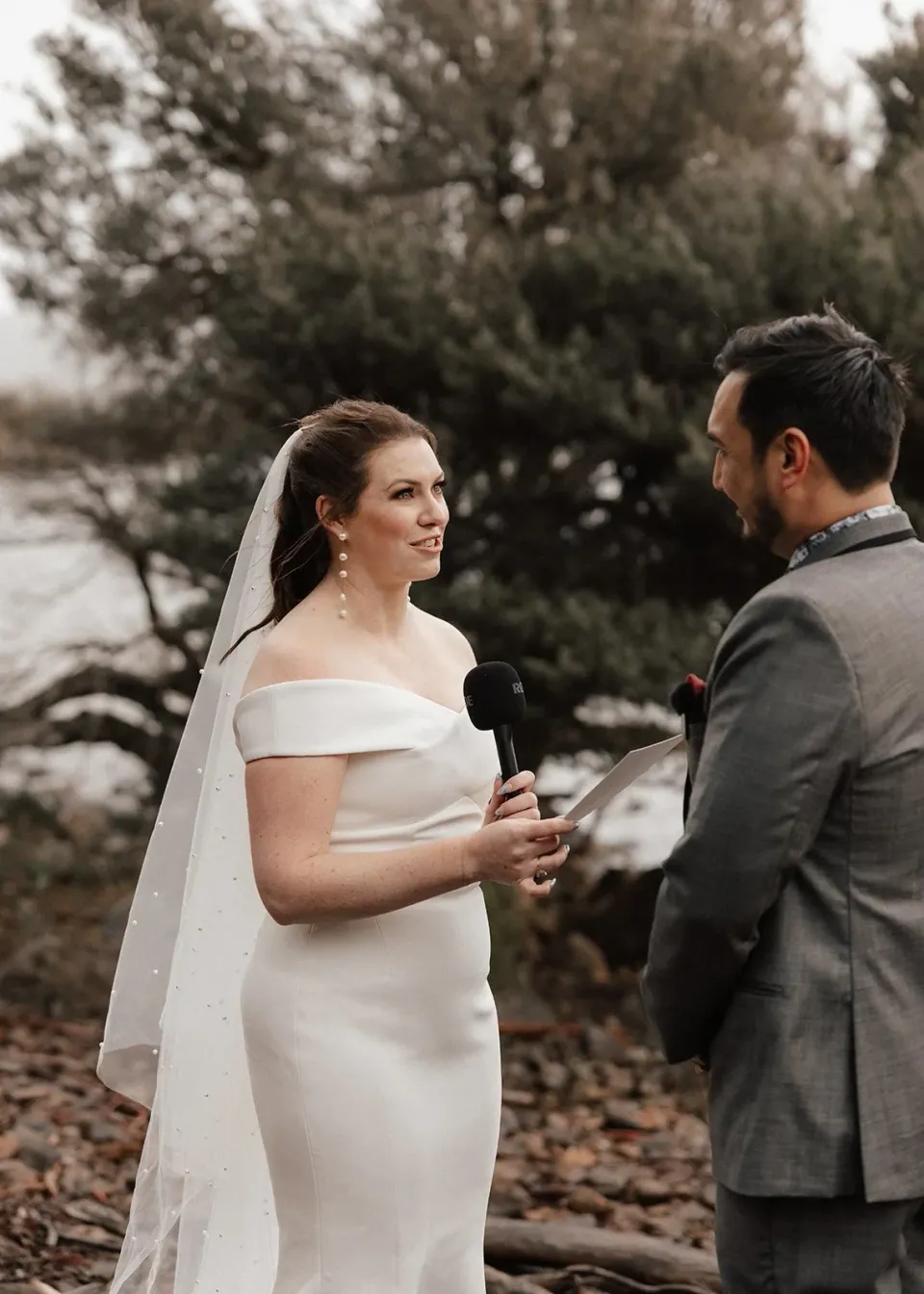 Sarah reading her vows to Jono on the rocky lakeshore, at Pumphouse Point, Lake St Clair, Tasmania, for an Elopement Collective elopement. Photo by Bulb Creative.