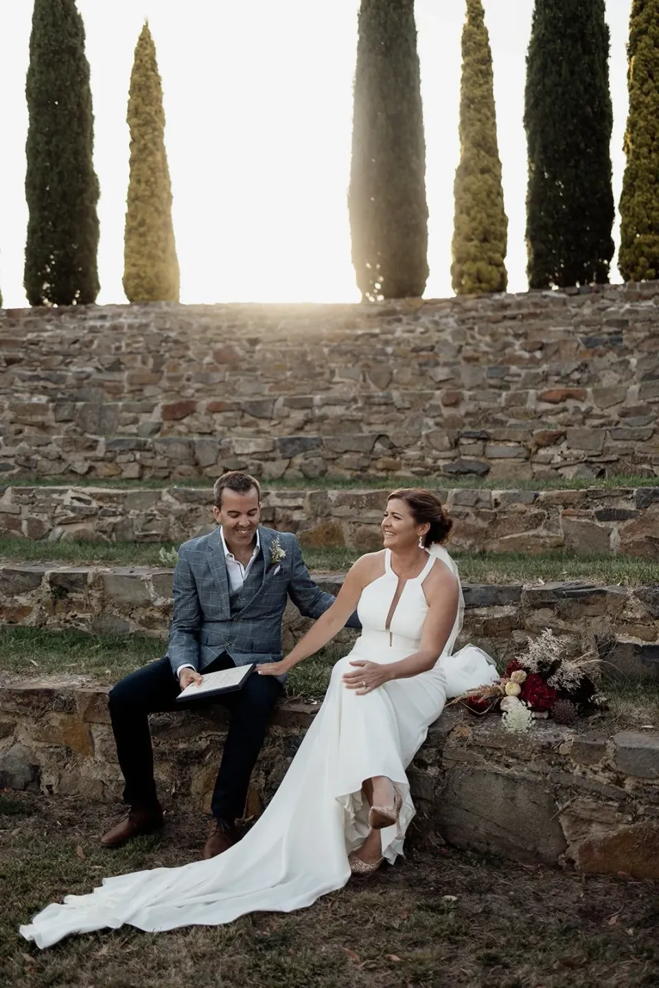 A couple sit together on stone steps, with the bride's train spread across the steps.