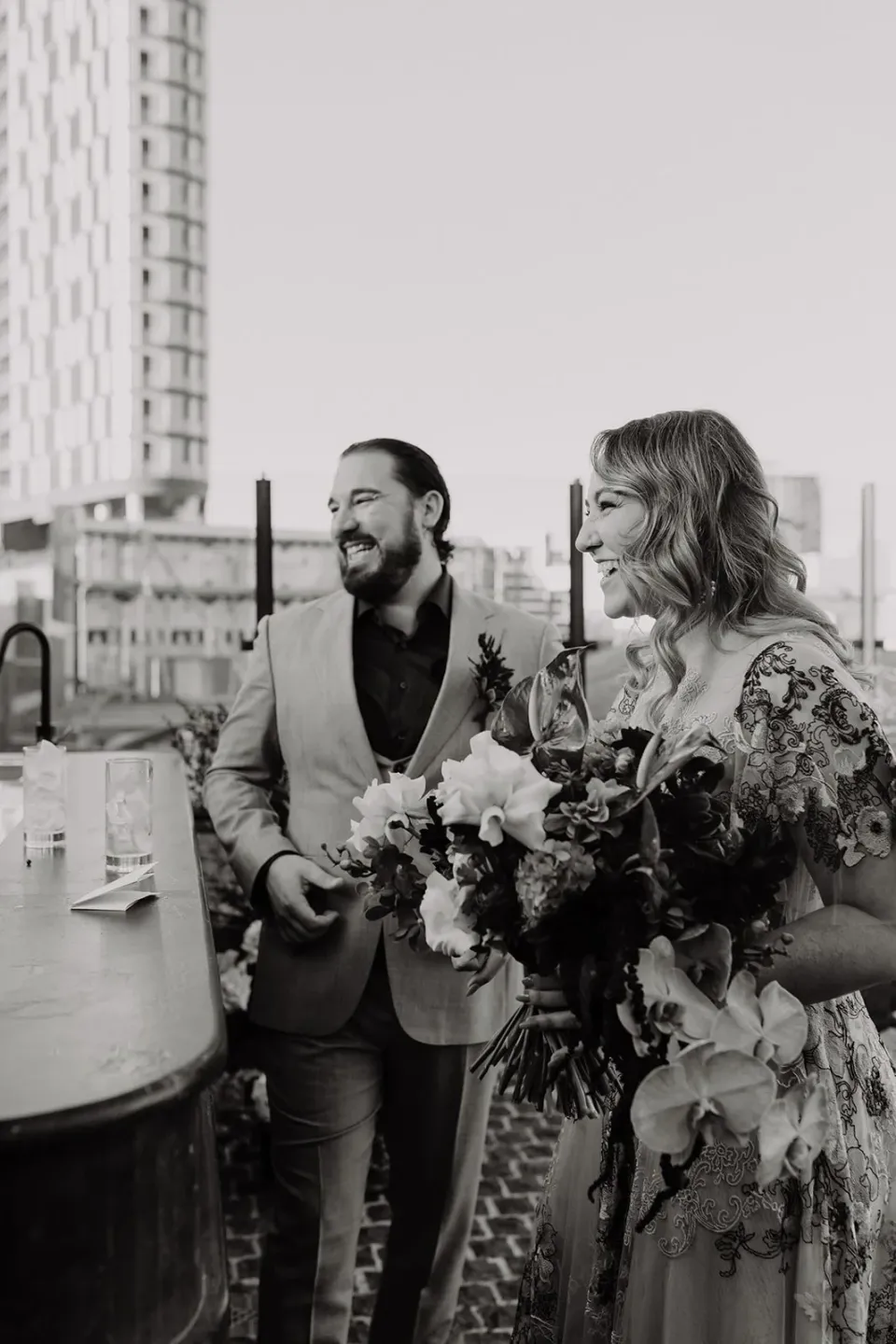 Black-and-white portrait of Victoria and Daniel on the rooftop terrace with her bouquet by Mrs Gibbons Flowers, at Agnes Restaurant in Fortitude Valley, Brisbane, for an Elopement Collective elopement. Photo by Tessa Shannon.