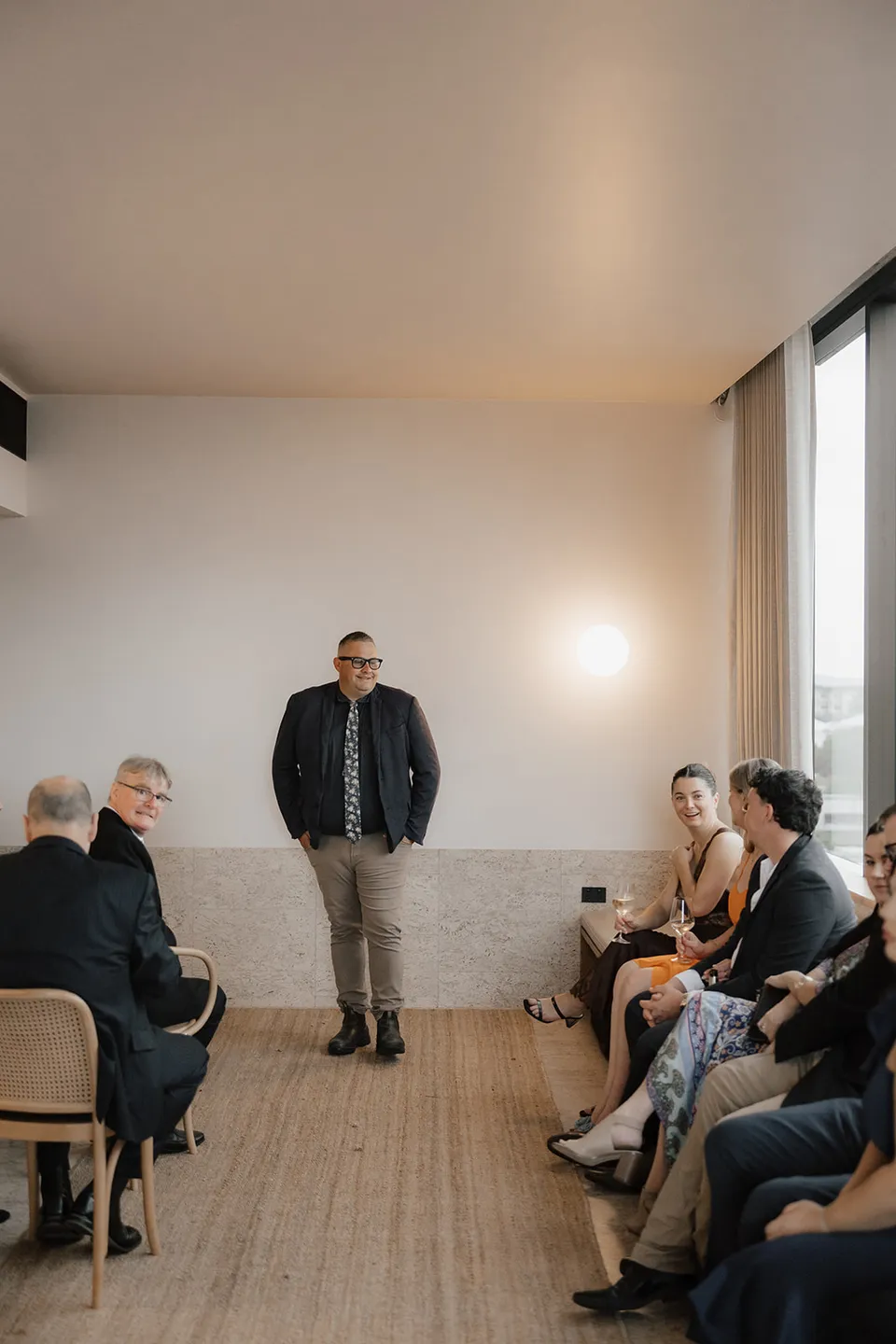 Celebrant Josh Withers leading Clare and Matt’s ceremony with guests seated in the suite, at The Calile Hotel in Fortitude Valley, Brisbane, for an Elopement Collective elopement. Photo by Harley from Bulb Creative.