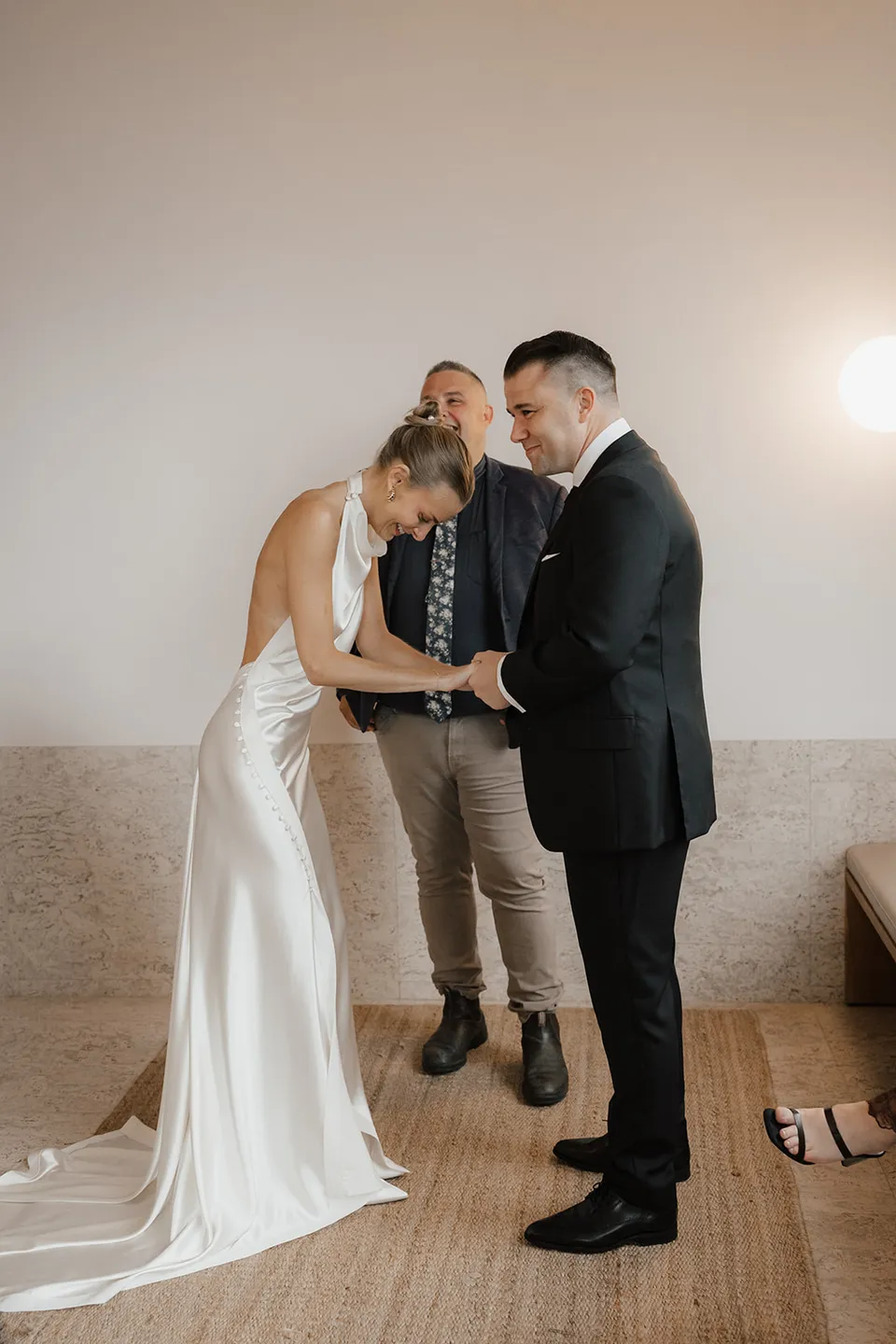 Clare looking down at their hands during the ring exchange, with celebrant Josh Withers behind them, at The Calile Hotel in Fortitude Valley, Brisbane, for an Elopement Collective elopement. Photo by Harley from Bulb Creative.